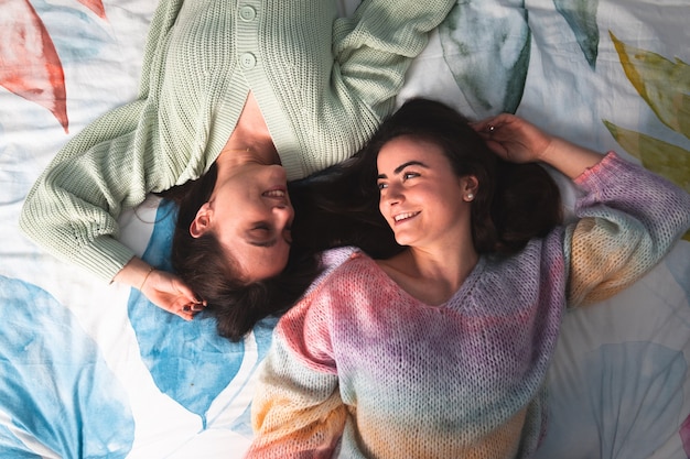 Photo two cute young women laying on a bed