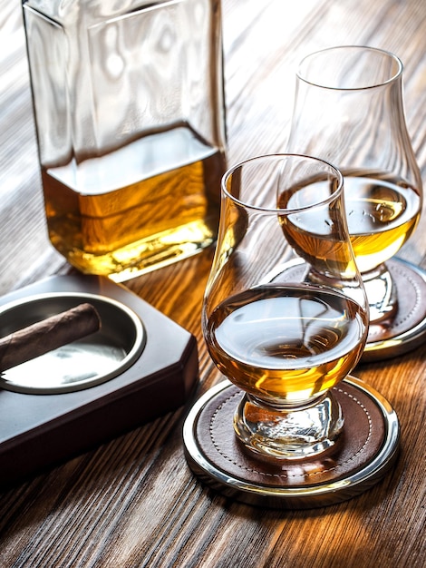 Two dams of whisky in glencairn glasses and a cigar in an ashtray