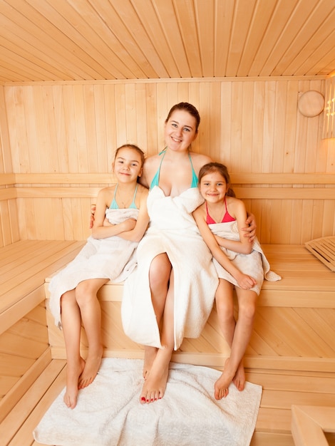 Two daughters with mother sitting on bench at sauna