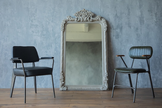 two decorative chairs and a mirror on a gray wall