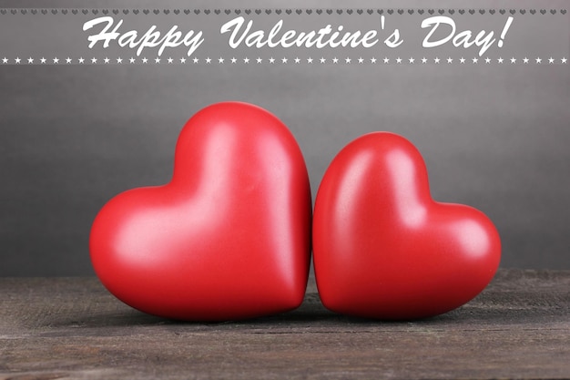 Two decorative red hearts on wooden table on grey background