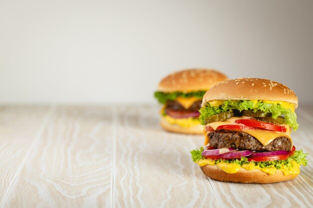 Two delicious burgers with meat, melted cheese, dripping sauce and vegetables on white wooden rustic background with space for text. Freshly made tasty hamburgers, close-up and copy space