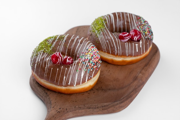 Two delicious chocolate donuts placed on a wooden cutting board. 