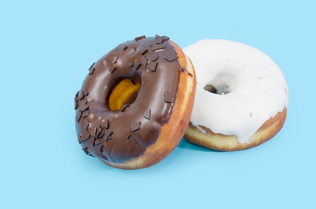 파란색 배경에 고립 된 검은 색과 흰색 초콜릿 입힌 두 맛있는 도넛