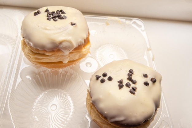 透明なプラスチック容器の白い背景に、粉砂糖とチョコレート チップを入れた 2 つのおいしいドーナツ