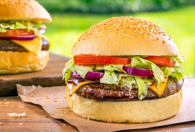 Two delicious Hamburgers on a wood desk with green grass nature.