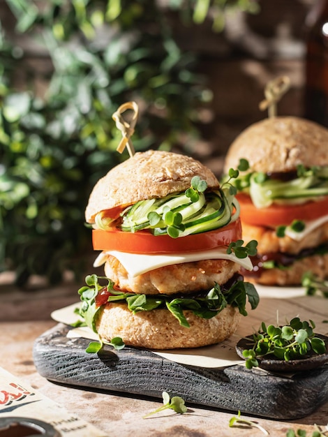 Two delicious homemade burgers of beef cheese and vegetables on wooden board at greenery background