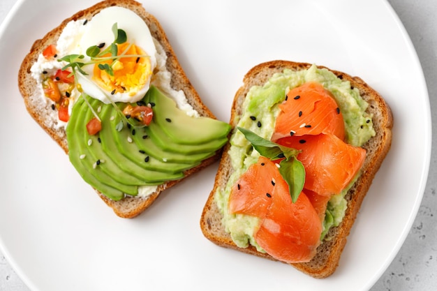 Two delicious sandwiches or healthy toast with avocado salmon\
basil eggs avocado toast top view