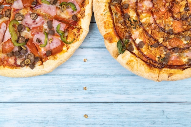 Two different delicious big pizzas on a blue wooden background