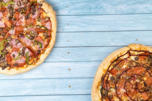 Two different delicious big pizzas on a blue wooden background