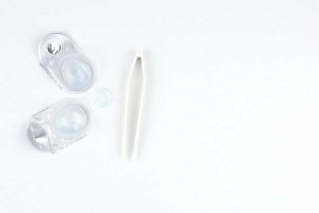 Two disposable contact lens containers and a contact blue soft lens and beige tweezers lie on the