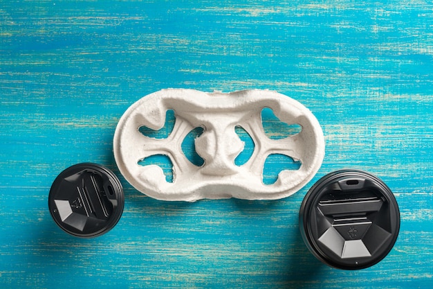 Two disposable paper cups of coffee and a disposable cup holder on a blue wooden surface