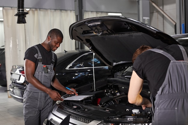 Two diverse auto mechanics cooperating while examining car engine