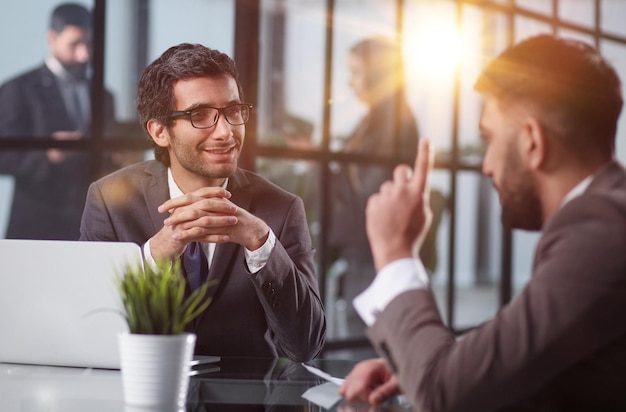 Two diverse colleagues discussing project strategy chatting during break sitting at table in office