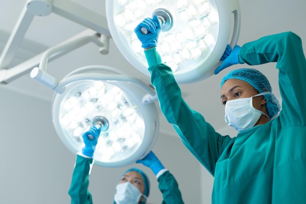 Фото Две разные женщины-хирурги настраивают освещение в операционной для операции с копировальным пространством. больничные, медицинские и медицинские услуги.