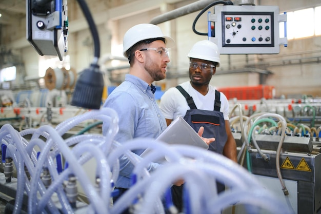 Photo two diverse professional heavy industry engineers wearing safety uniform and hard hats working on laptop