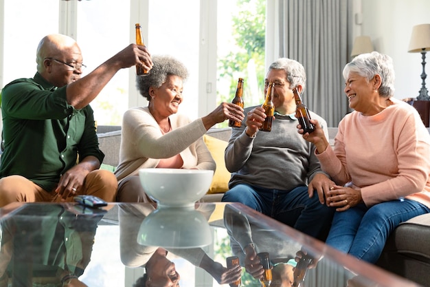 Photo two diverse senior couples sitting on sofa with beer and having fun