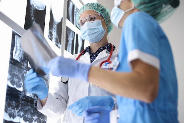 Two doctor in suits, medical gloves and protective masks hold X-ray photograph