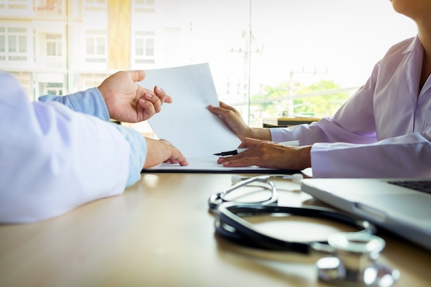 Two doctors discussing patient notes in an office pointing to a clipboard with paperwork as they make a diagnosis or decide on treatment