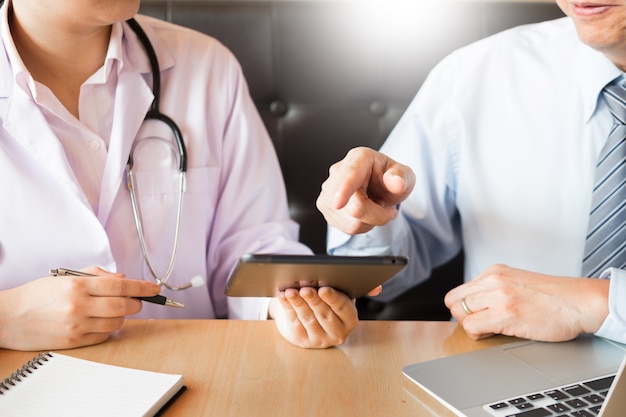 Two doctors discussing patient notes in an office pointing to a tablet 