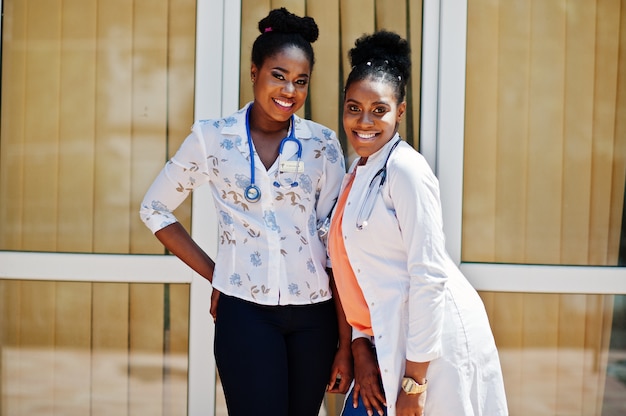 Two doctors female at lab coat with stethoscope posed outdoor against clinic