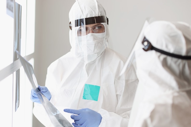 Two doctors in protective suits and goggles are discussing an xray of patient