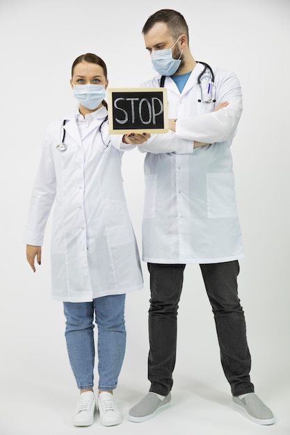 Two doctors in white lab coat and protective mask holding a stop sign