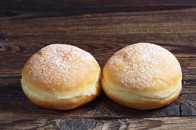 Two doughnuts with powdered sugar on dark wooden table