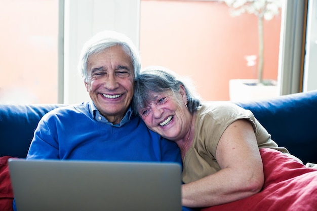 Two elderly people are sitting at home at the weekend surfing the net buying online watching movies senior couple using laptop