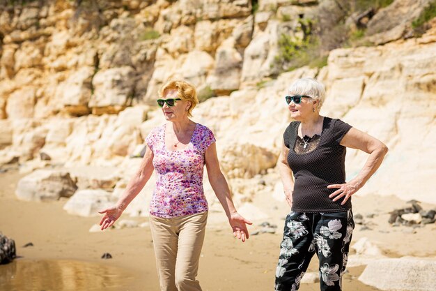 2 人の年配の女性が岩の多い海岸に沿って歩いています。