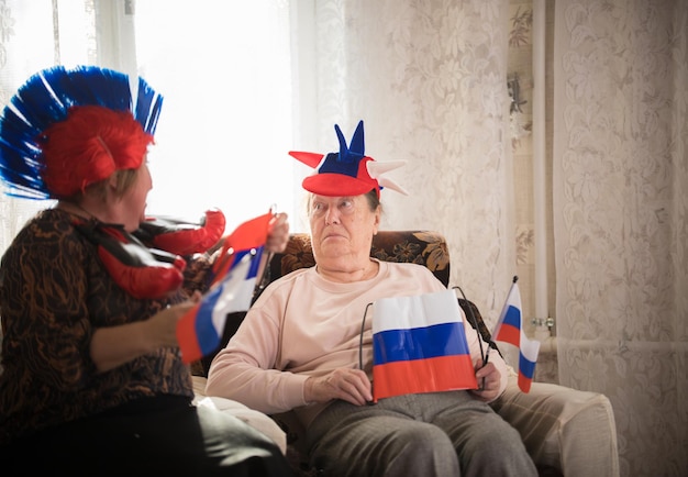 Two elderly women sitting in russian accessories holding russian flags