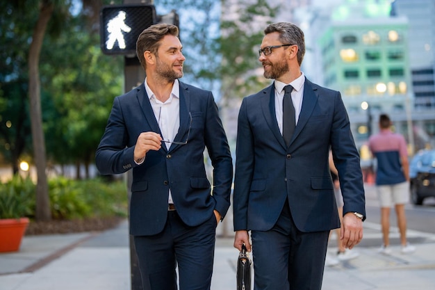 Two elegant businessmen walking outdoors together in the streets with office building business men w