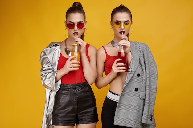 Two elegant glamor hipster twin girls in fashion red top with cocktail drink