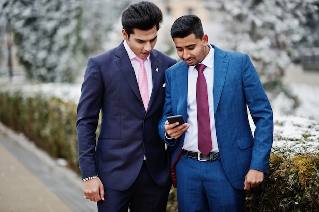 携帯電話を見て冬の日に提起されたスーツの2つのエレガントなインドのファッショナブルなマンモデル。