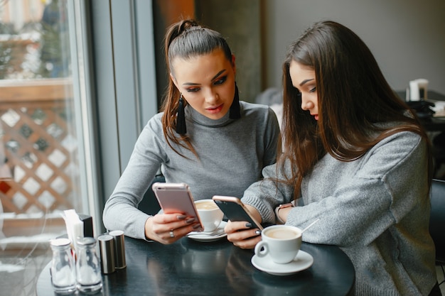 two elegant and magnificent girls sitting in a cafe and drinking a coffee