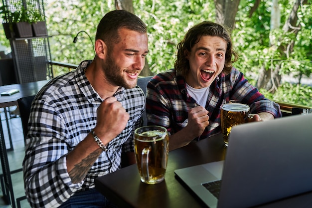 Foto due uomini emozionati che guardano il calcio in un pub e bevono birra.