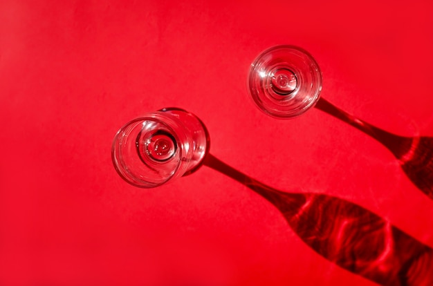 Two empty glasses with shadows on red background in natural sunlight