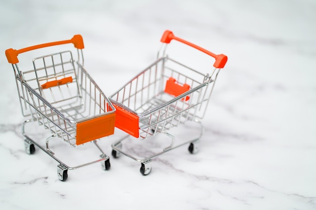 Two empty metal small miniature toy shopping trolley on white marble background. Shopping, supermarket, sale concept. Collection of shopping carts.