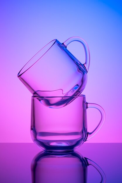 Two empty tea cups on a pink and blue neon background. drinking glass. dark silhouette, night illuminated effect. glassware. transparent tableware, dishes