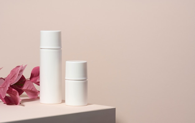 Two empty white plastic tubes for cosmetics stands on a wooden podium on a beige background with a shadow. Containers for cream, shampoos, liquid substances. Branding, template