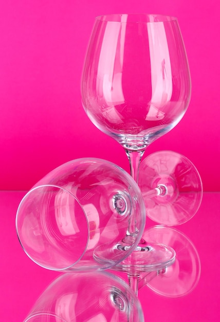 Two empty wine glasses on color background