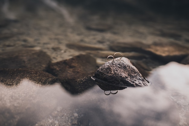 Foto due semplici anelli d'oro di fidanzamento su uno stand su una pietra grigia dall'acqua cristallina