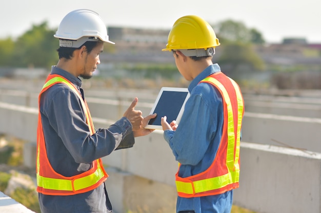 通信を話す2人のエンジニアが建設現場でタブレット検査を使用