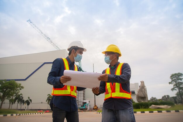 Two engineer teamwork working blueprint on site construction,Engineer wear face mask protect covid19,worker work architect professional