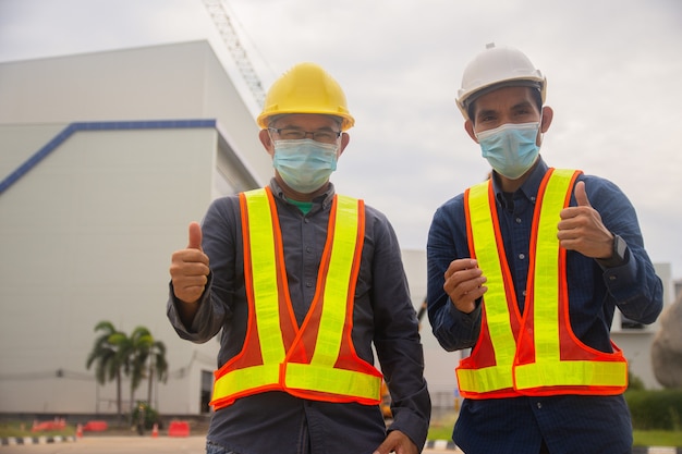 Два инженера добились успеха на строительстве объекта, два человека в медицинской маске защищают коронавирус covid19, рабочий, работающий архитектор