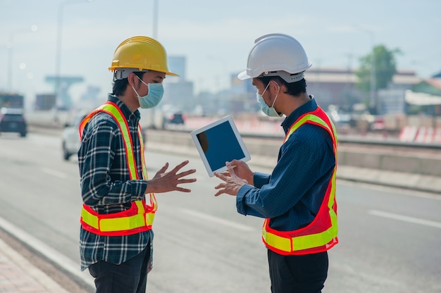 Two engineer wear face mask using tablet work outdoor on site survey