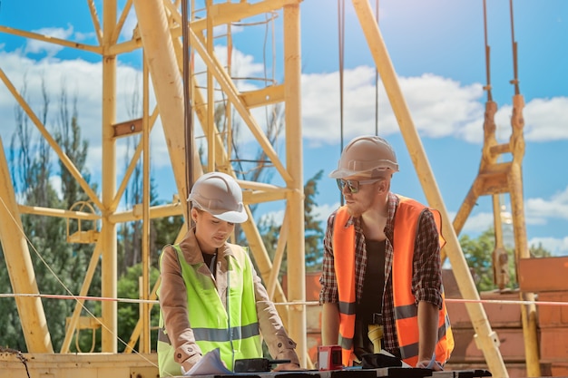 Two engineers discuss the construction process according to a drawing against the  of a construction tower crane