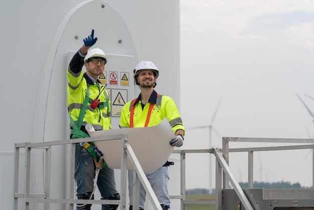 風力発電所の風力タービンの検査とメンテナンスのための設計図を持つ 2 人のエンジニア