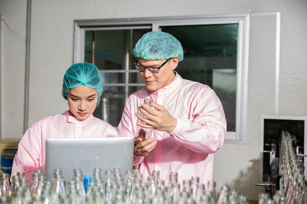 Two engineers oversee quality control checking product bottles on a beverage factorys conveyor belt