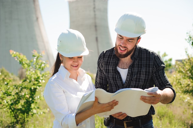 Two engineers standing at electricity station, discussing plan.